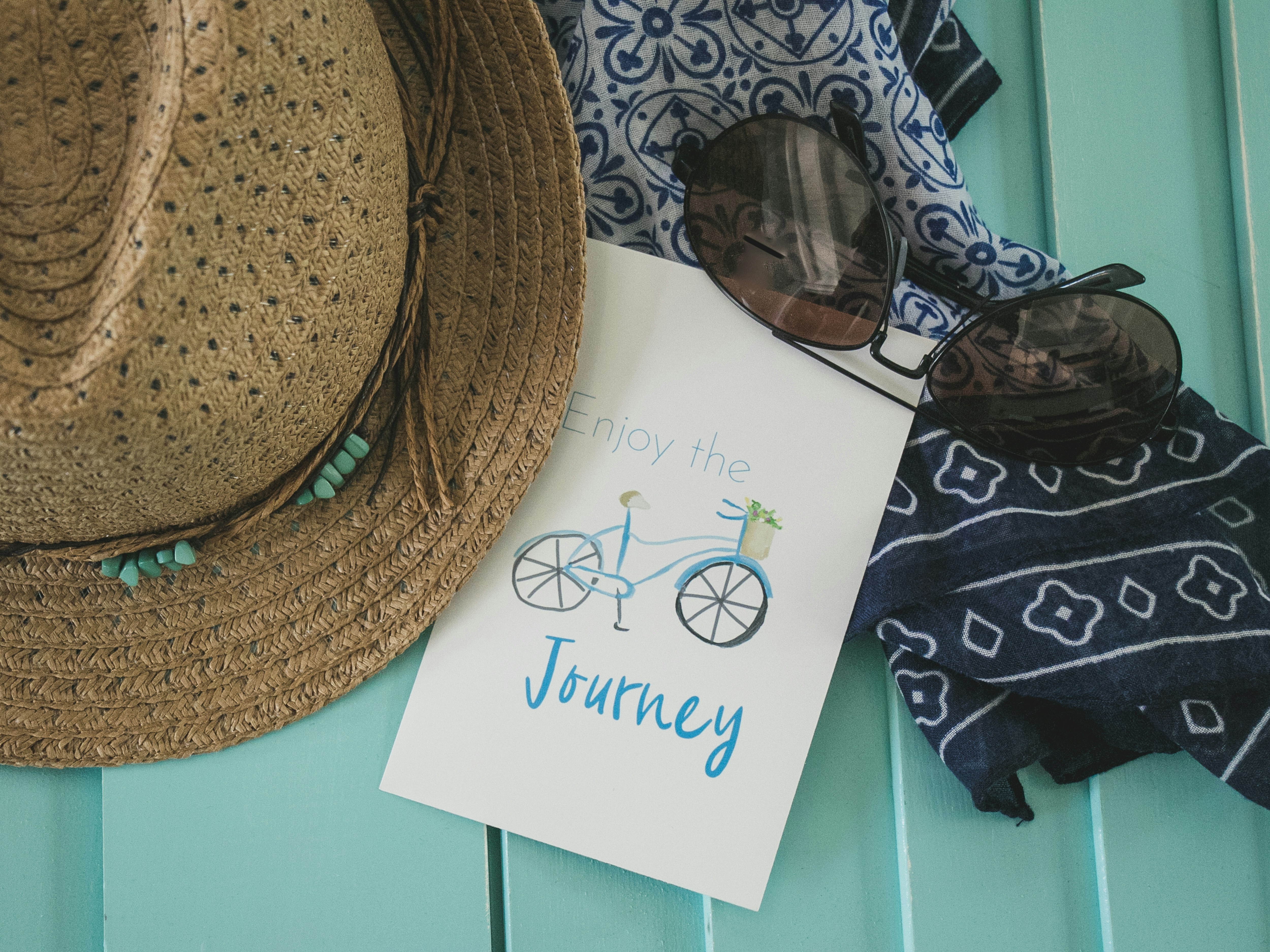 a hat, sunglasses, scarf, and card stating "enjoy the journey" regarding self-care and travel